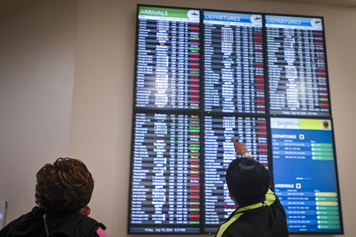 Passengers check the board displaying delayed flight information due to the global communications outage caused by CrowdStrike